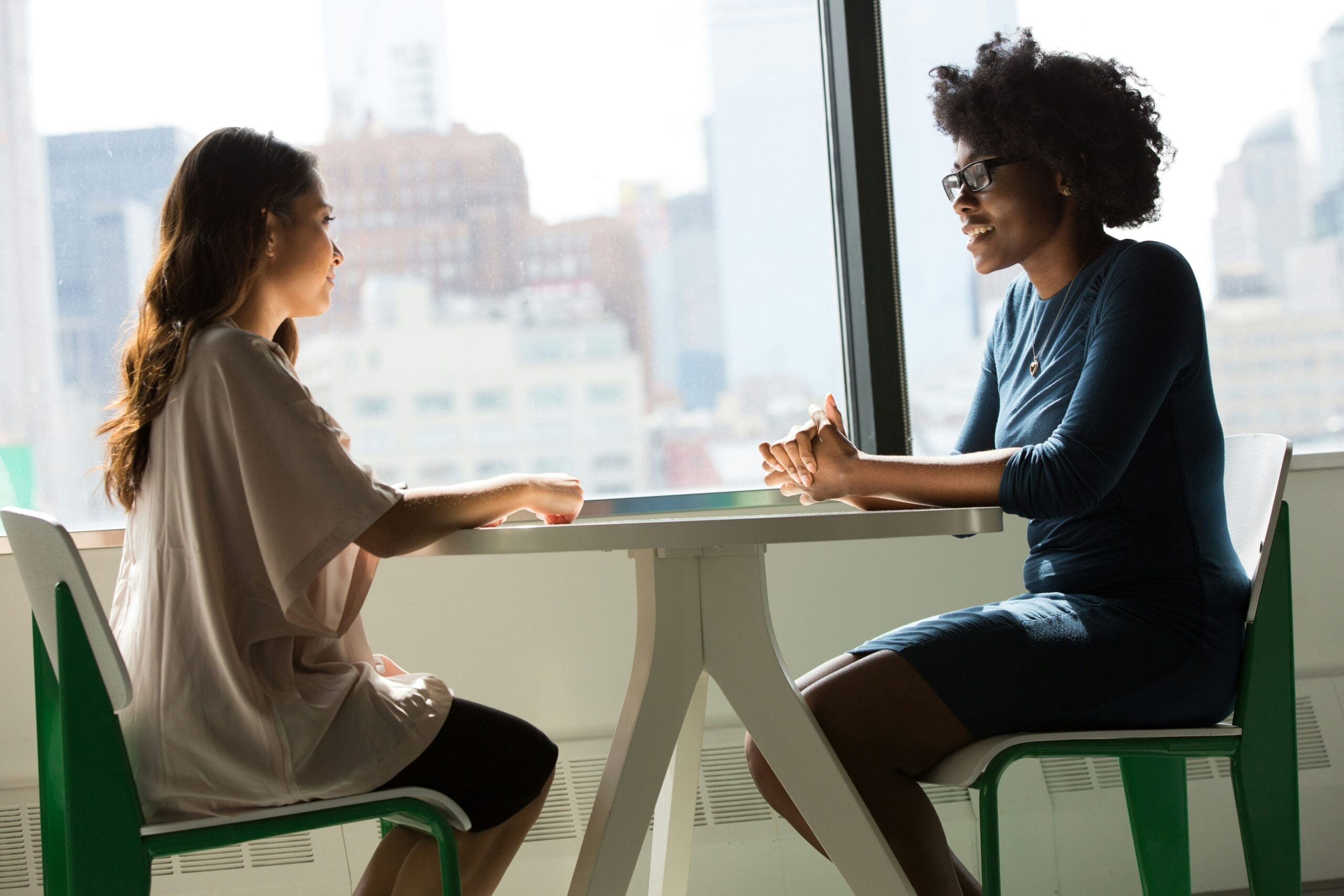 Two women sitting a cafe in front of large pane-glass window, deep in conversation.