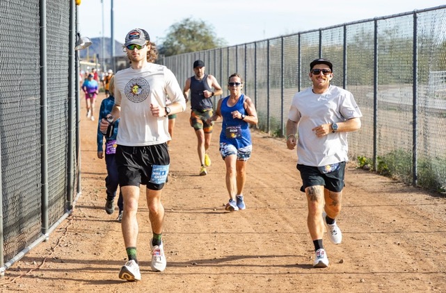 Grayson, an ACP fundraiser, running in an ultra-marathon with a baseball hat, white shirt and blue shorts, with other runners around him.