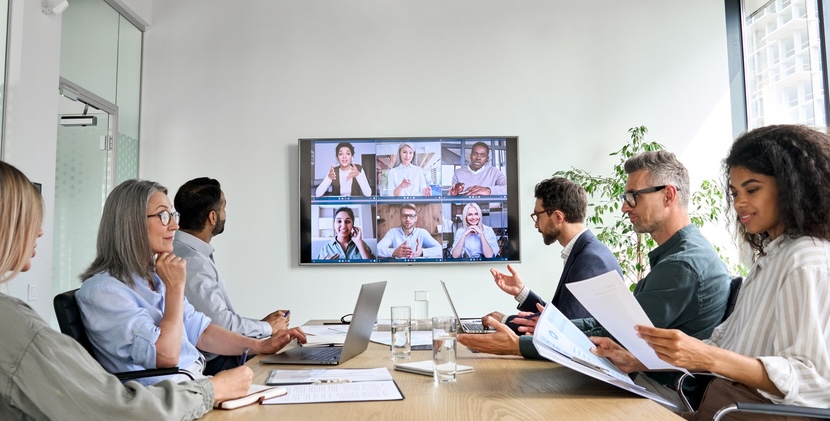 Six people sitting around a conference table engaging on a video call with participants.