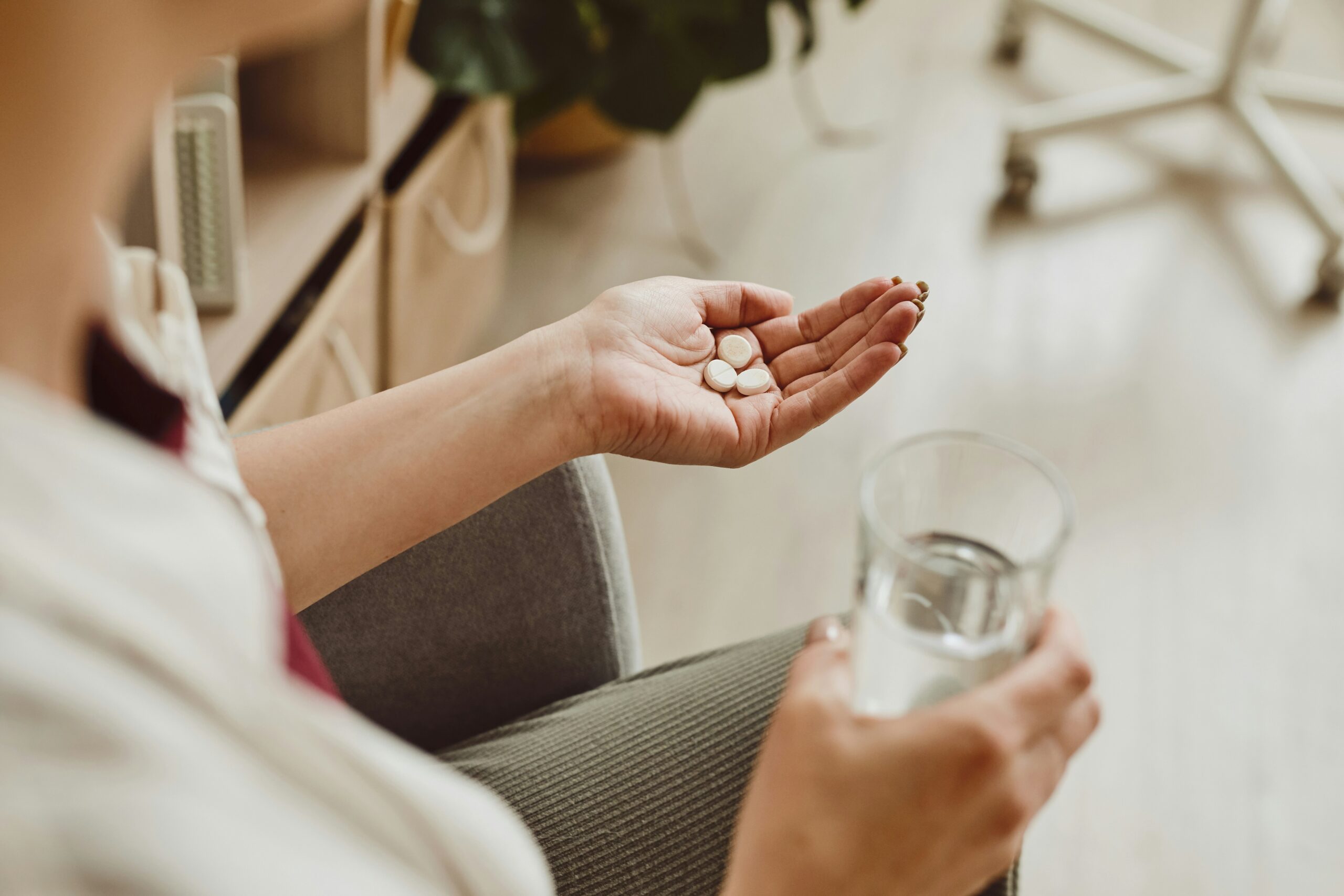 CLose up of a person's hand holding meds in the left hand and a glass of water in the right hand.