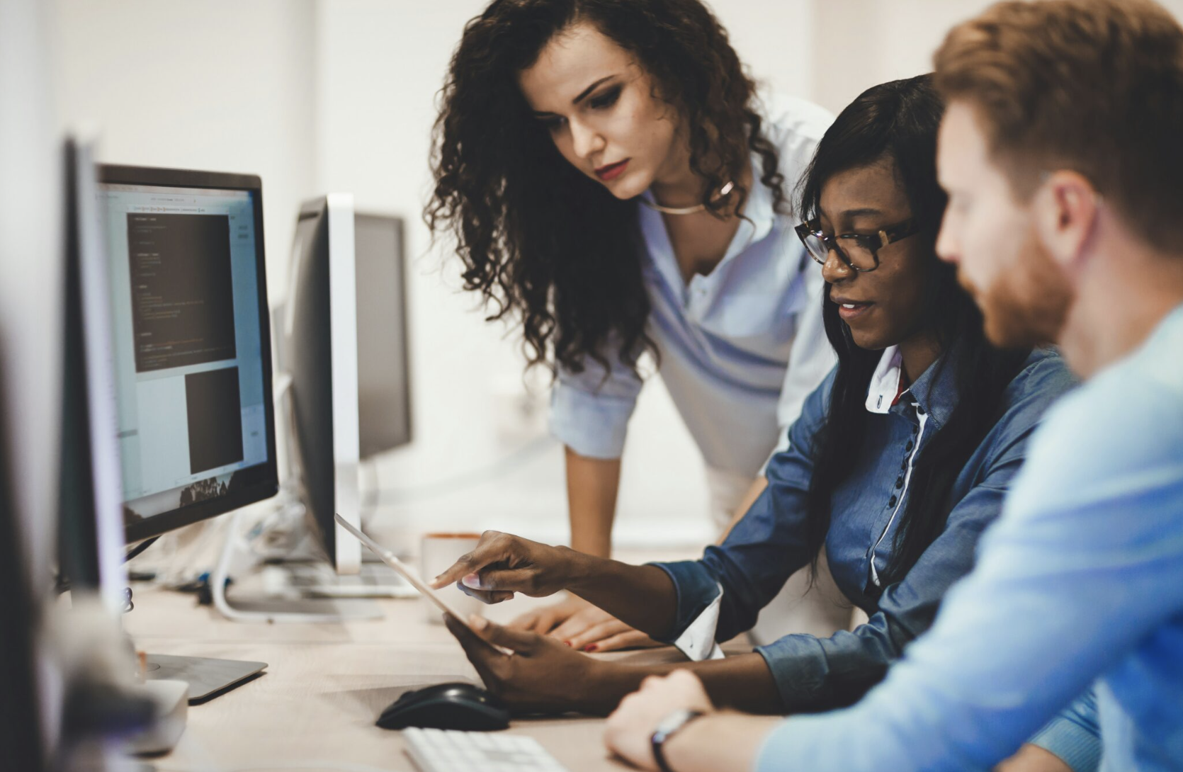 A small team of researchers huddled around computer screen analyzing data one of them is holding on a clipboard.