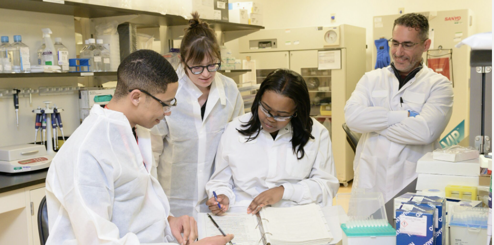 A team of researchers in a lab circled together in discussion.