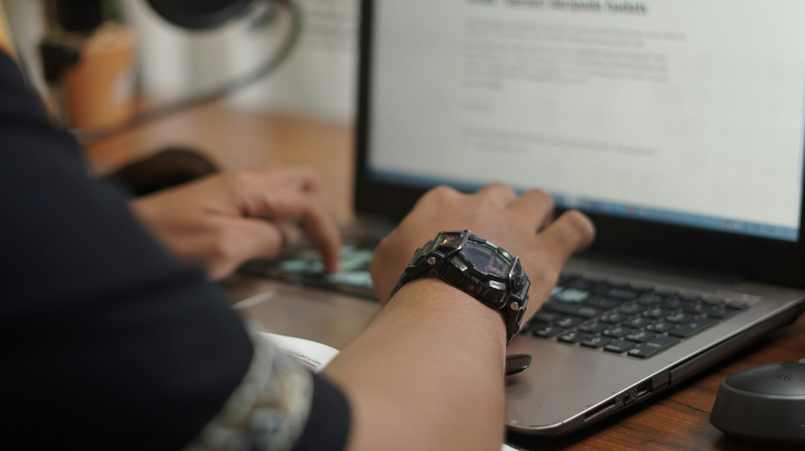 Close up of a man wearing a black sports watch typing on a laptop.