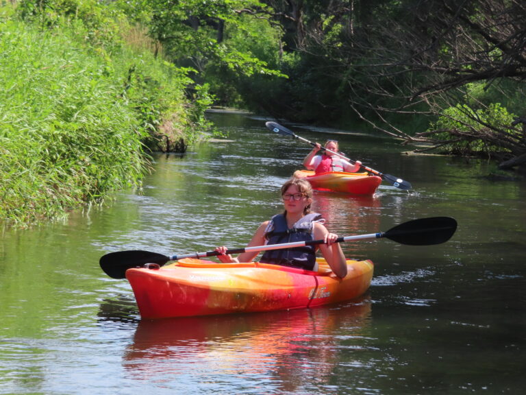 Two campers canoe down a river in kayaks.