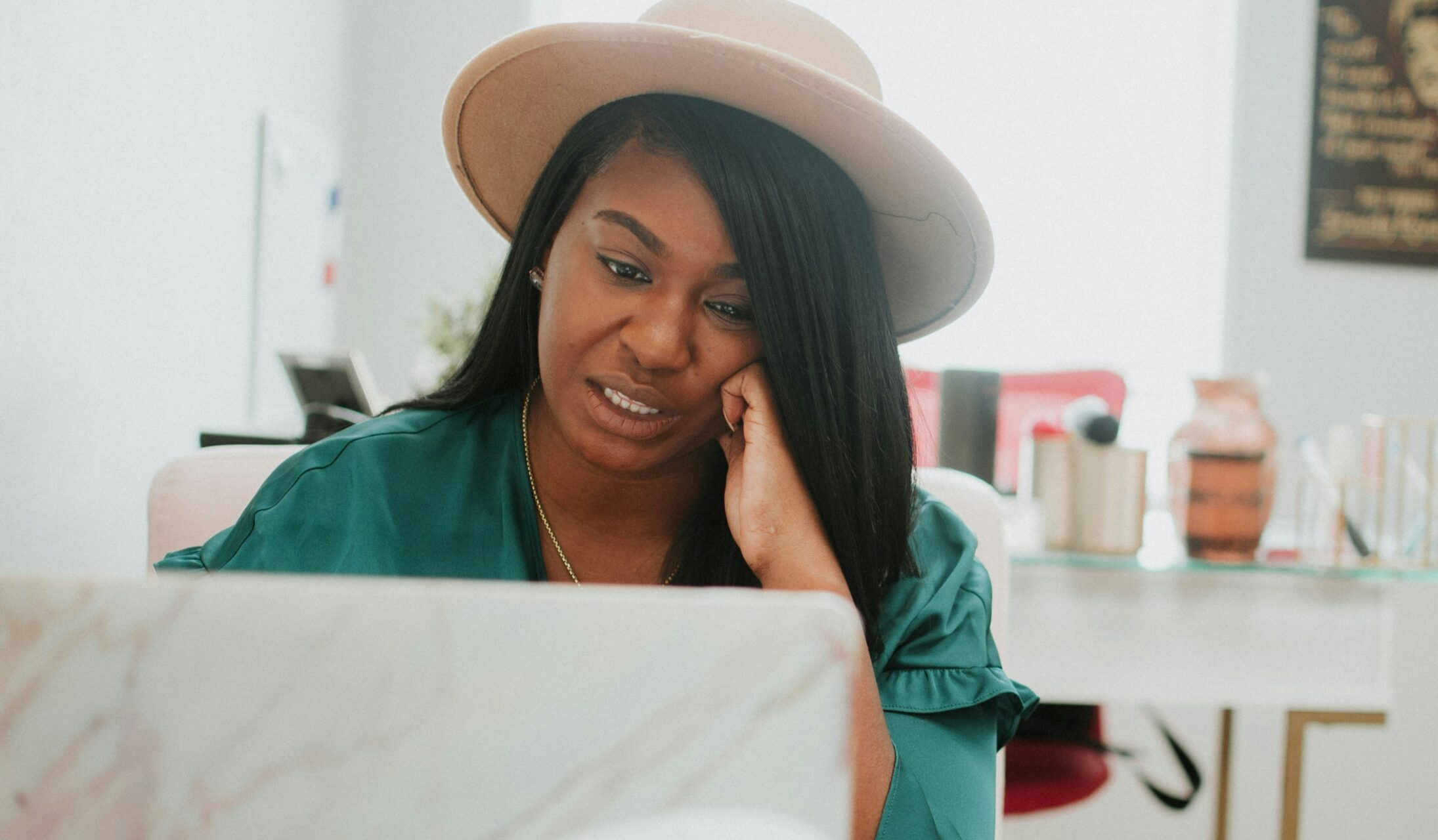 Black woman working on a laptop, resting her head on one hand.
