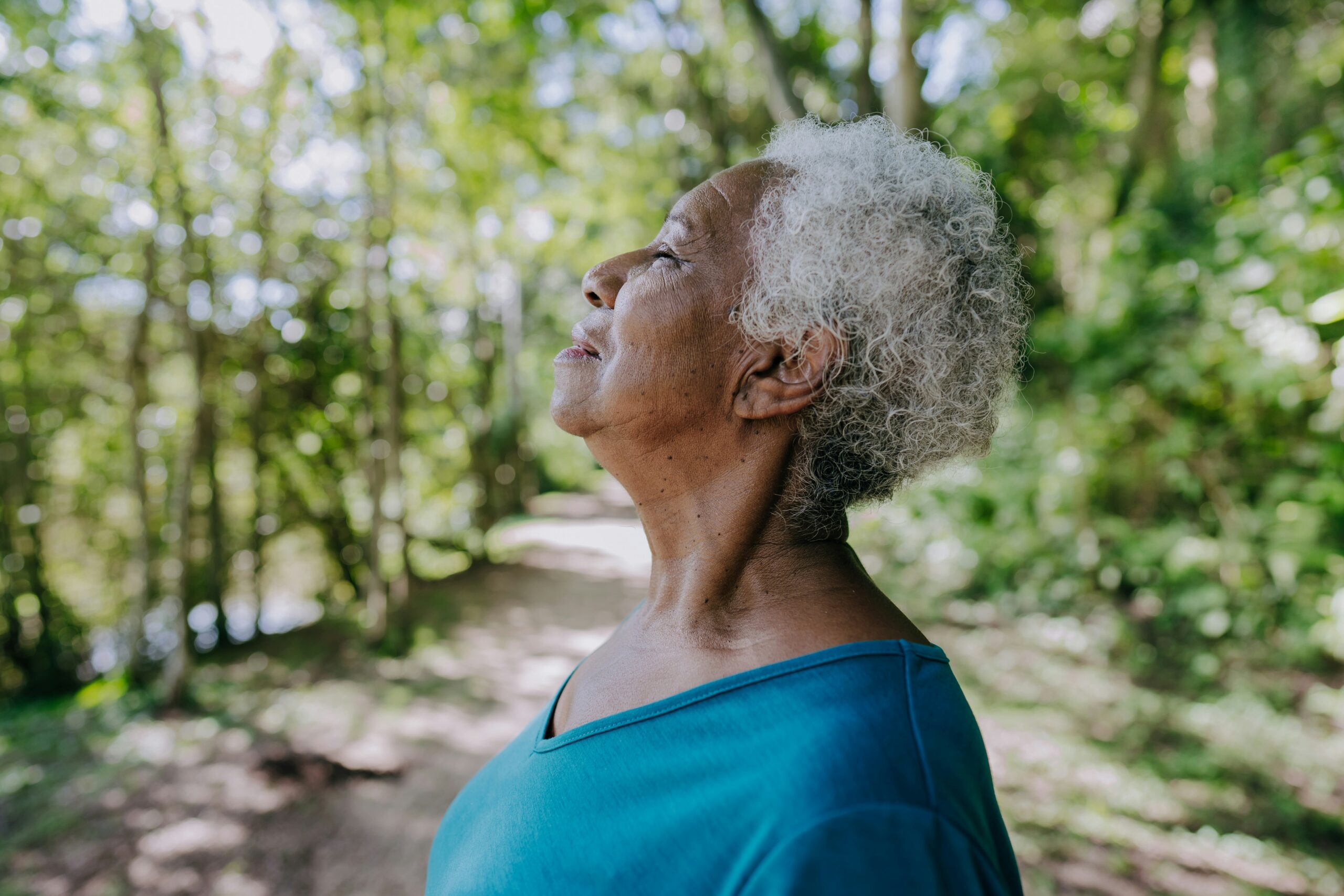 Older Black woman takes a moment of reflection on a wooded path.