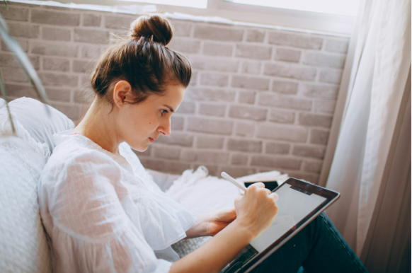 A woman sitting on her couch filling out a survey on a computer tablet