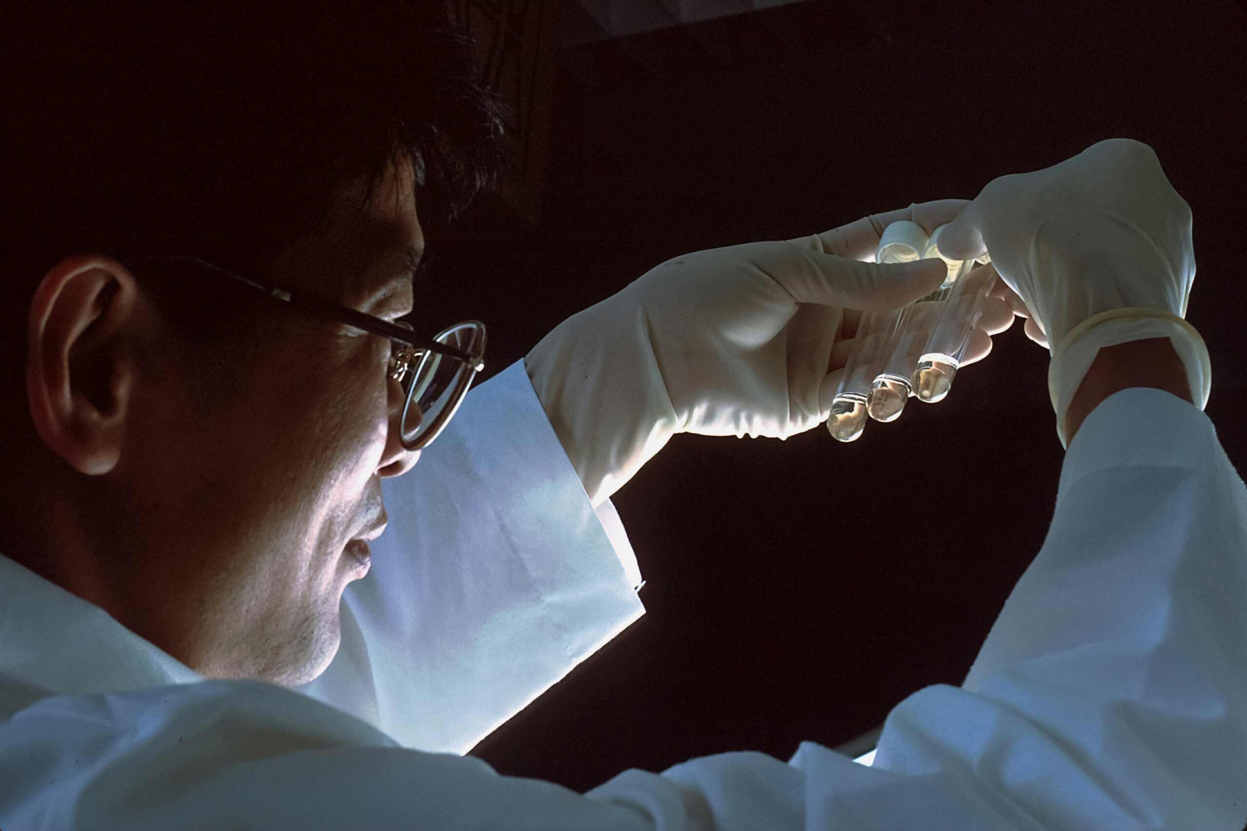 Male scientist holding up a lab slide against a dark background.