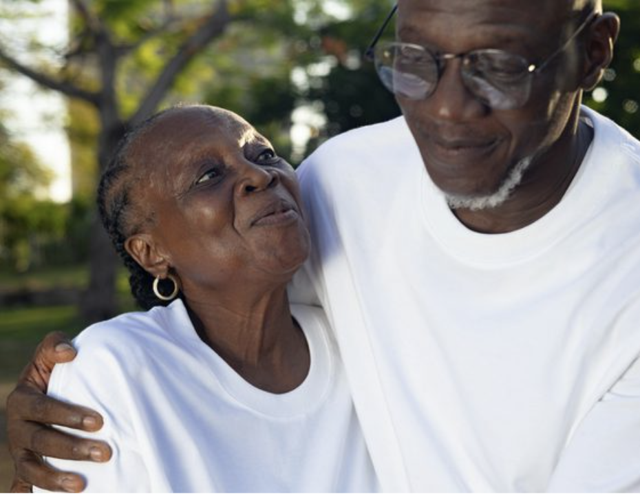 An older Black couple wearing white t-shirts in an outdoor park